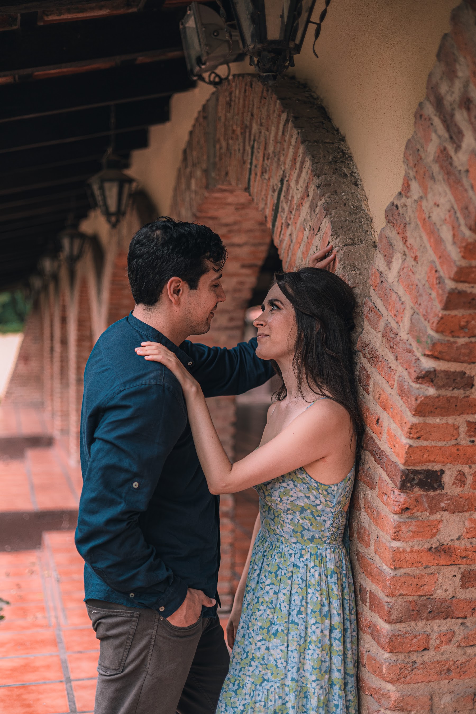 Arcelia y Adolfo se abrazan junto a un muro de ladrillo.