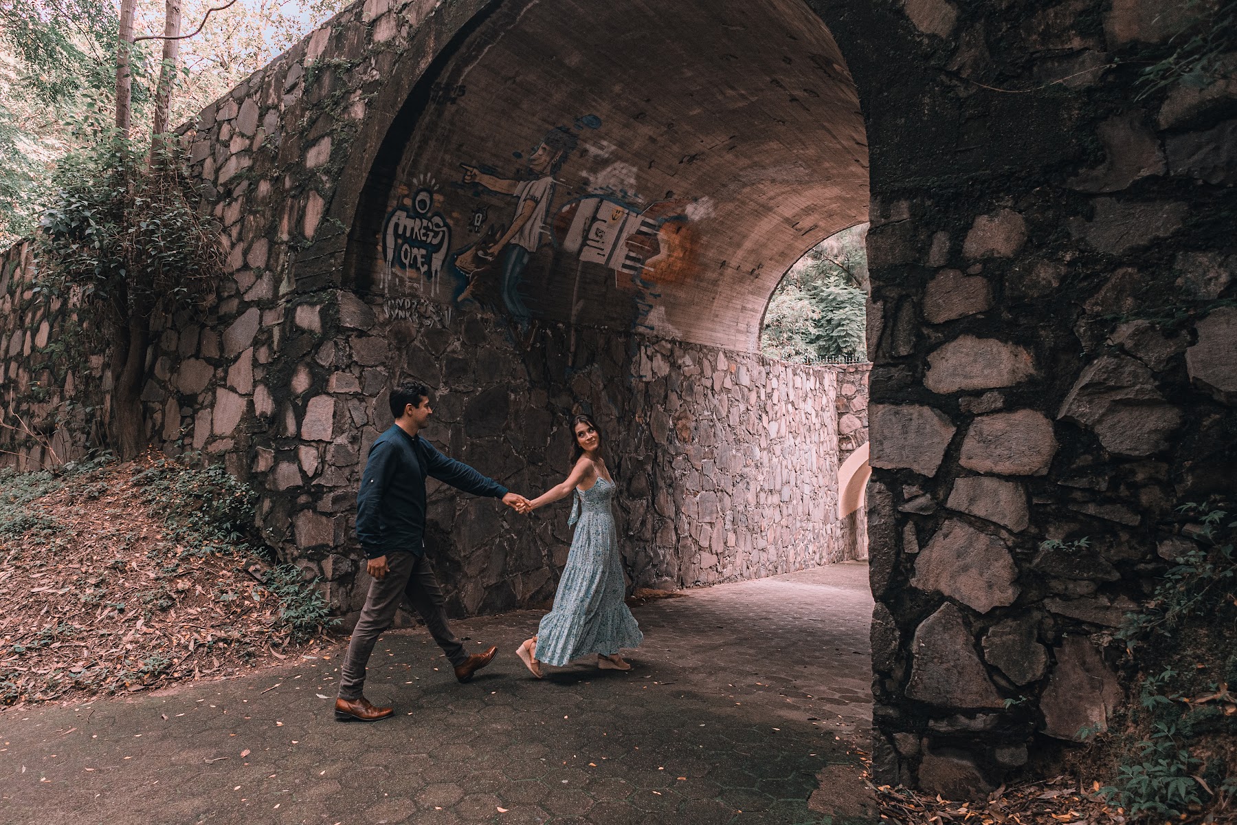 Los novios caminan de la mano bajo un arco de piedra.