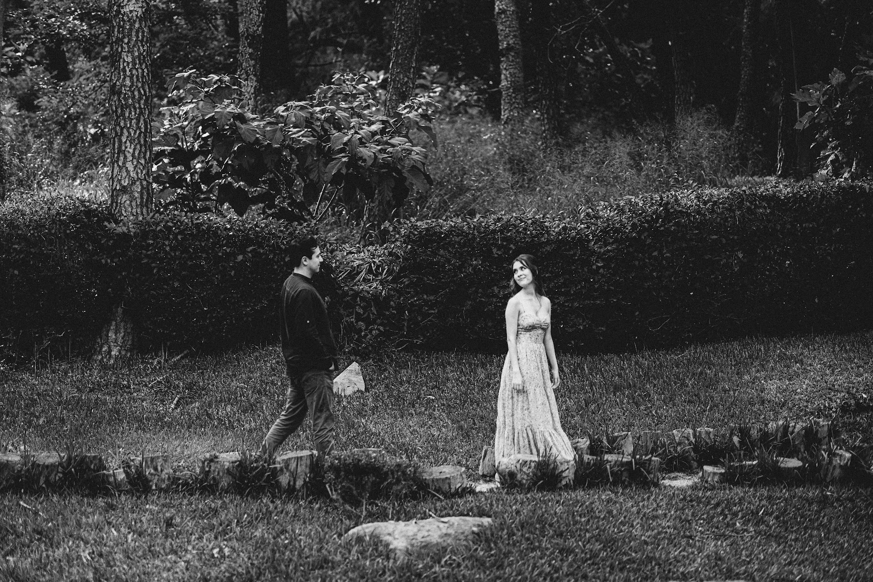 La pareja posa a distancia entre árboles en blanco y negro.