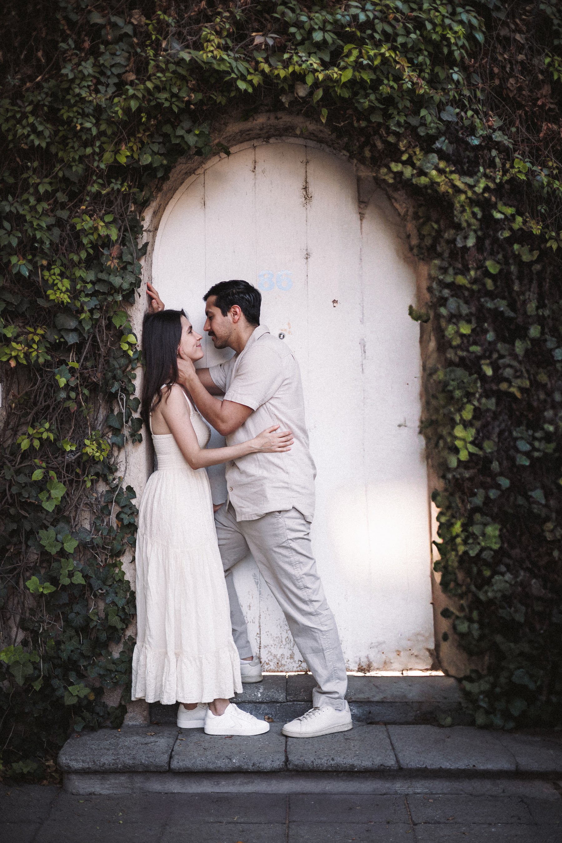 La pareja se besa junto a un muro cubierto de vegetación.