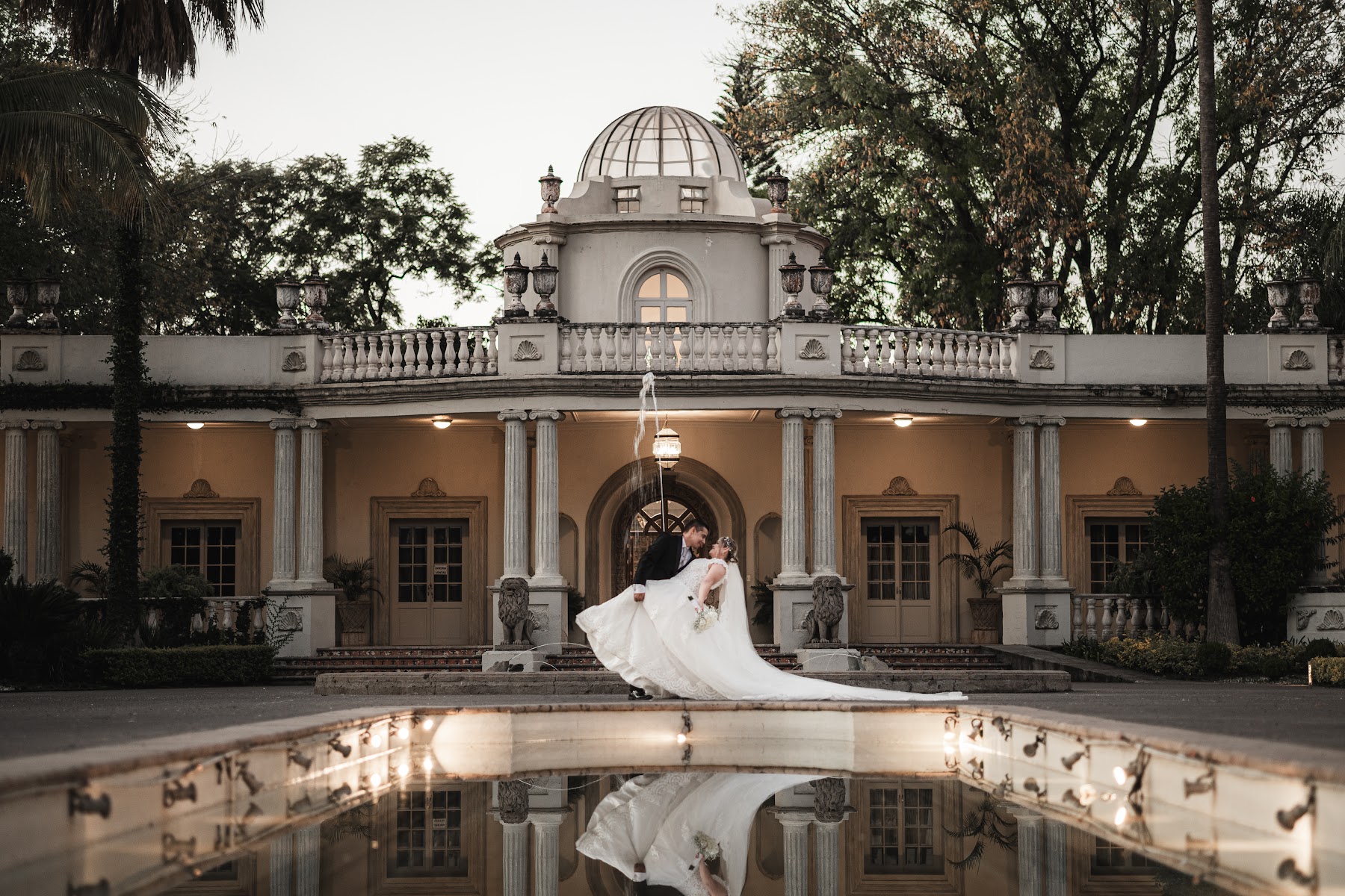 Los recién casados posan frente a una casona reflejada en el agua.
