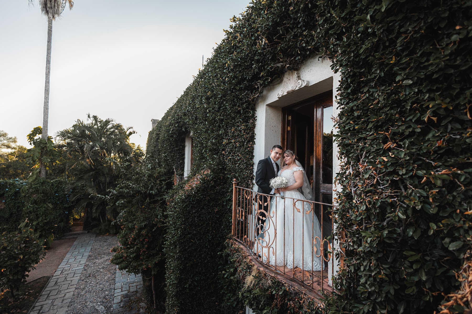 Los novios posan en un balcón rodeado de vegetación.