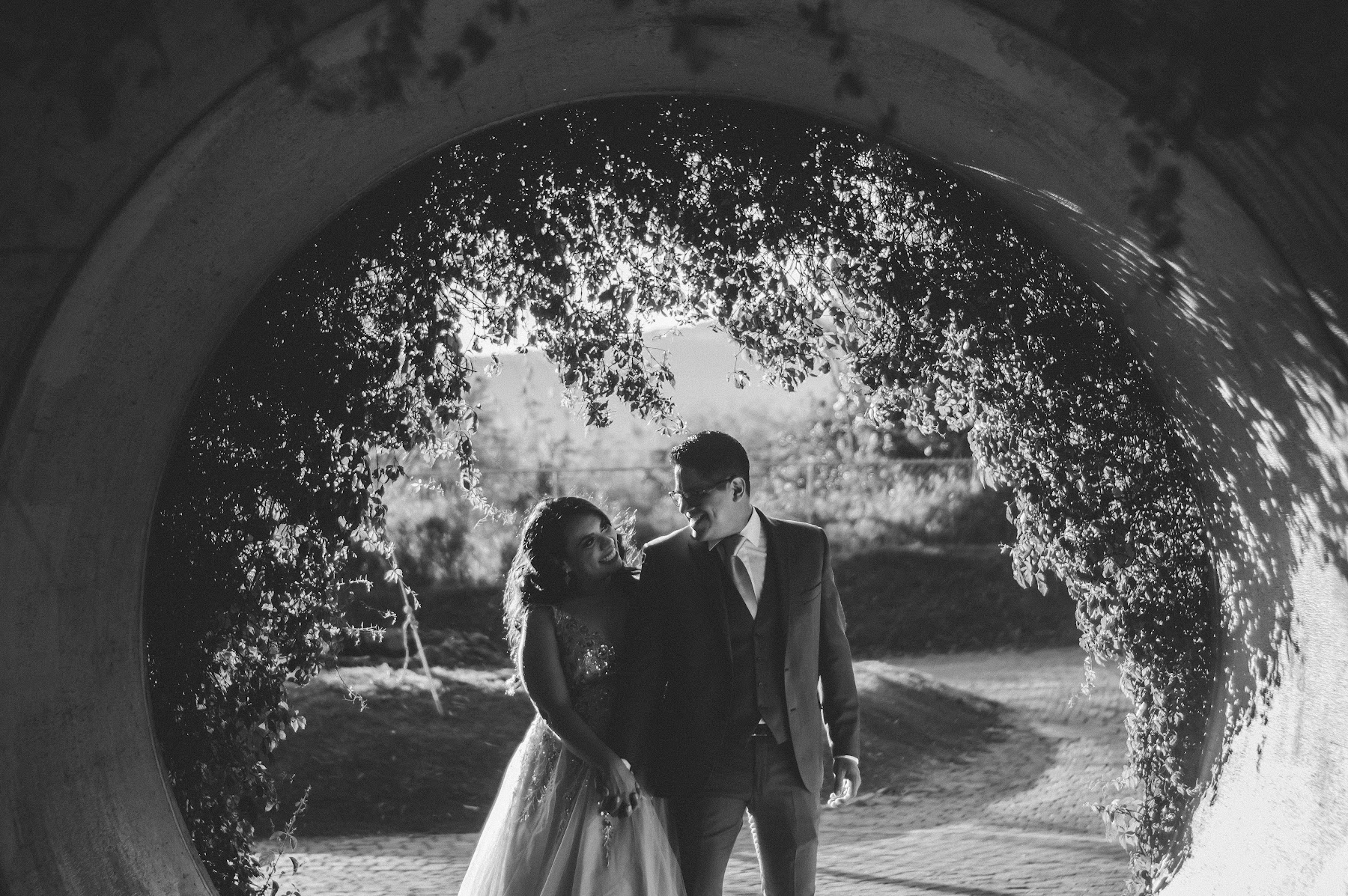 Los novios se miran bajo un arco en una toma monocromática.