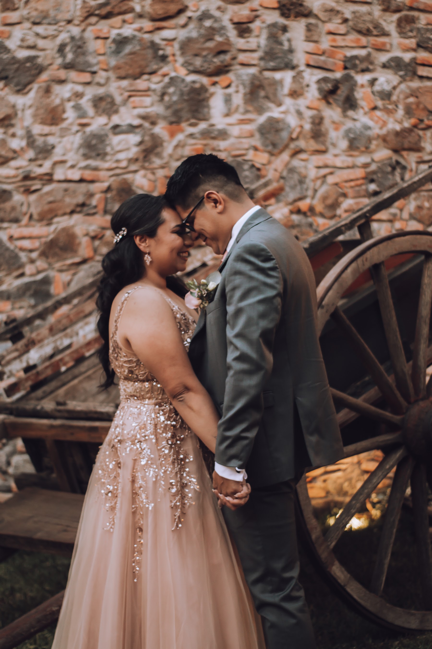 La pareja comparte un retrato frente a un muro de piedra.