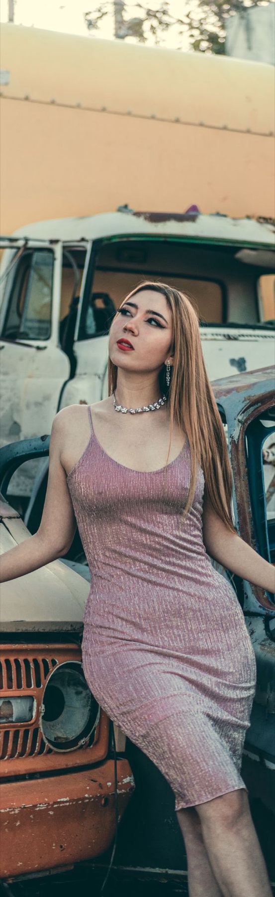 Mujer con vestido claro posando junto a un vehículo vintage