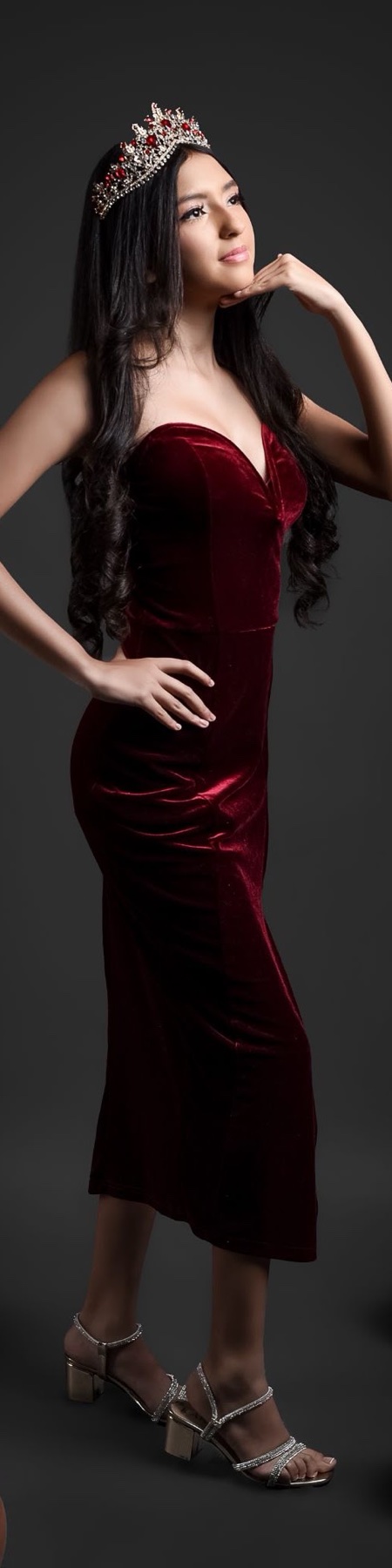 Quinceañera con vestido color vino y tiara sobre fondo oscuro