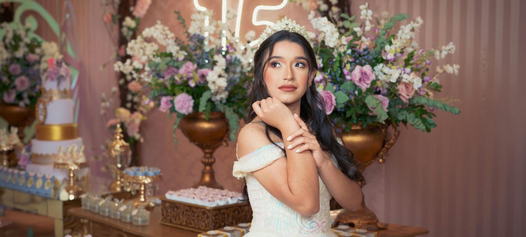 Quinceañera con vestido blanco frente a un arreglo floral de fiesta