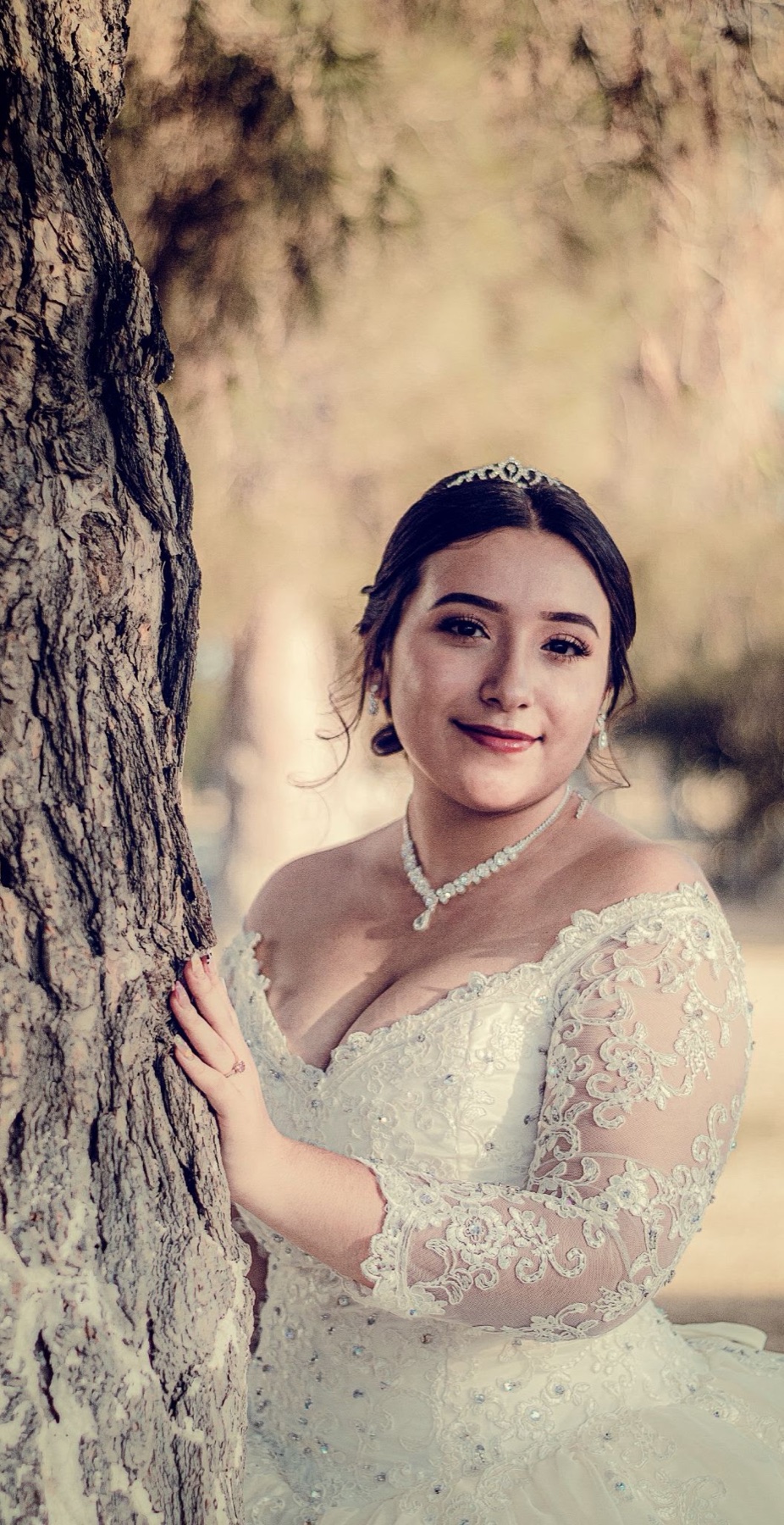 Retrato de quinceañera con vestido blanco junto a un árbol